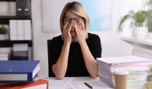 A stressed office worker rubbing her eyes, overwhelmed with paperwork, needing effective stress management techniques.
